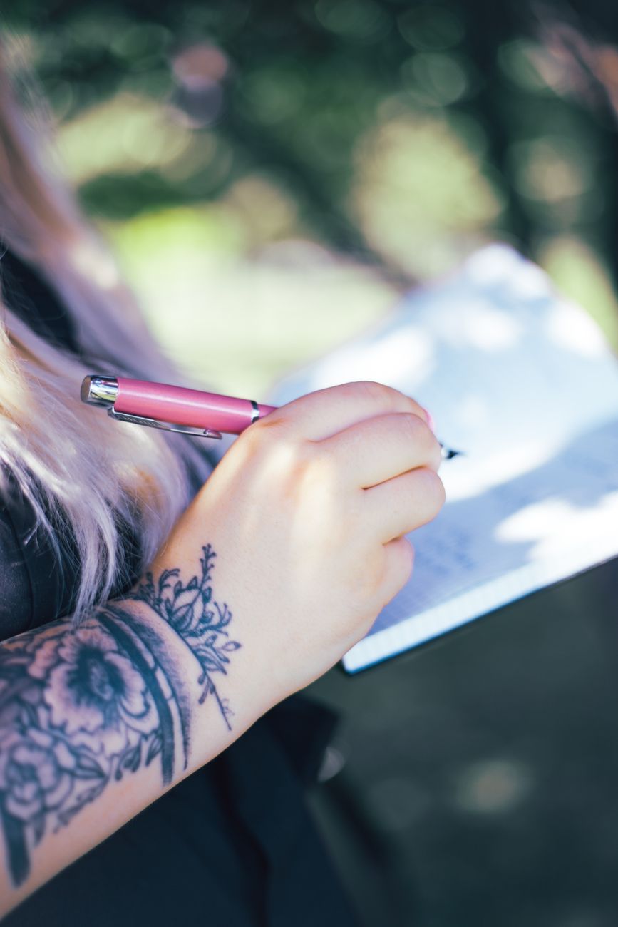 tattooed hand of woman writing outdoors. Photo by Kitty S on Pexels.com